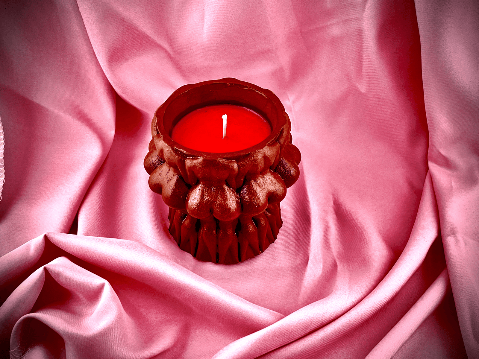 Dark brown concrete naked women circle candle from Lucentius resting on luxurious pink silk fabric, unlit, sculptural design visible