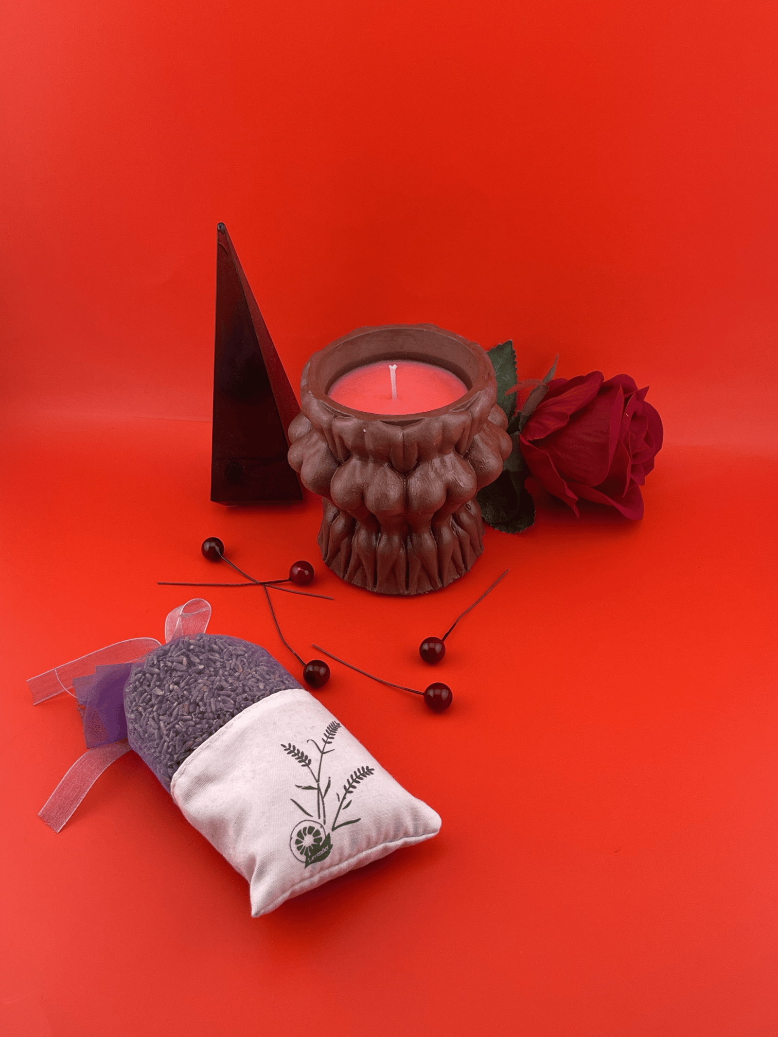 Naked women circle dark brown jar candle from Lucentius on red background next to black translucent pyramid and bag of aroma herbs, mystical and playful decor setting