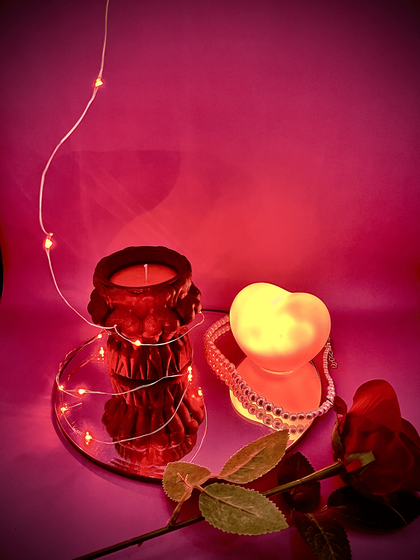 Naked women circle dark brown jar candle from Lucentius on round mirror next to illuminated heart and red rose on red background, romantic playful atmosphere